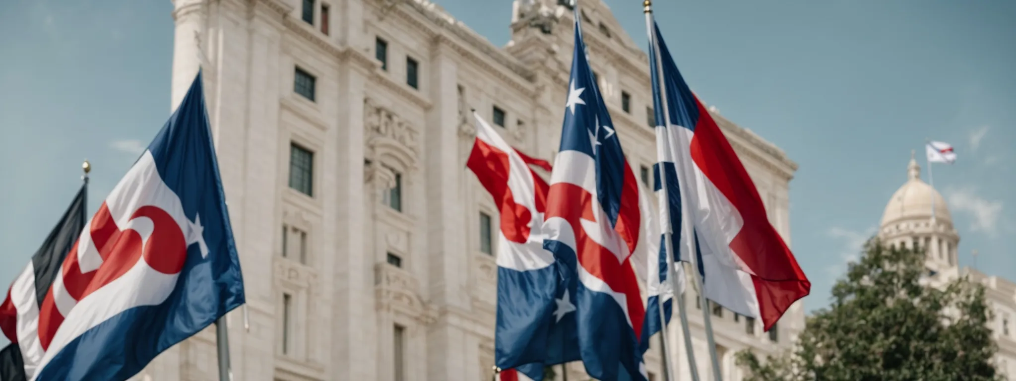 two national flags fluttering side by side against a backdrop of large, imposing government buildings under a clear sky.